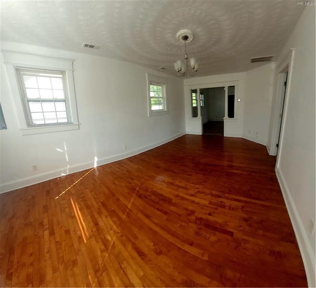 spare room with an inviting chandelier, a textured ceiling, visible vents, wood finished floors, and baseboards