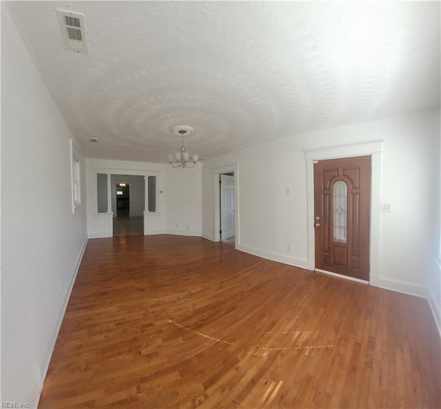 foyer entrance with light wood finished floors, a notable chandelier, baseboards, and visible vents