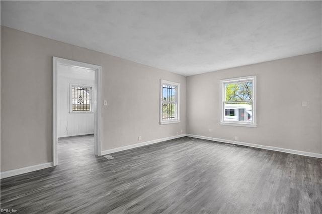 empty room featuring plenty of natural light, baseboards, and dark wood finished floors