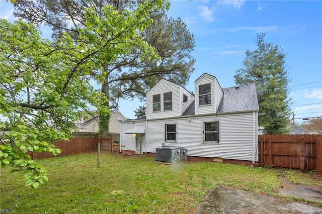 back of house with roof with shingles, a fenced backyard, central AC unit, and a lawn