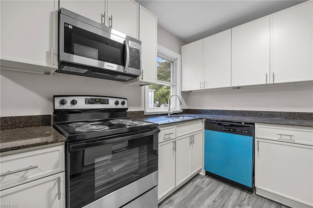kitchen featuring white cabinets, a sink, light wood finished floors, dark stone counters, and stainless steel appliances