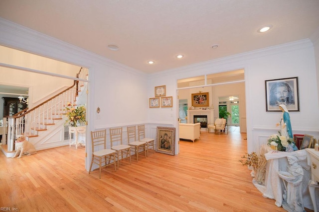 corridor with wainscoting, light wood finished floors, ornamental molding, and stairs