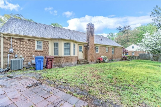back of house with a chimney, brick siding, central AC unit, a yard, and fence