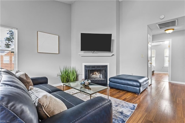 living area featuring a fireplace with flush hearth, visible vents, baseboards, and wood finished floors