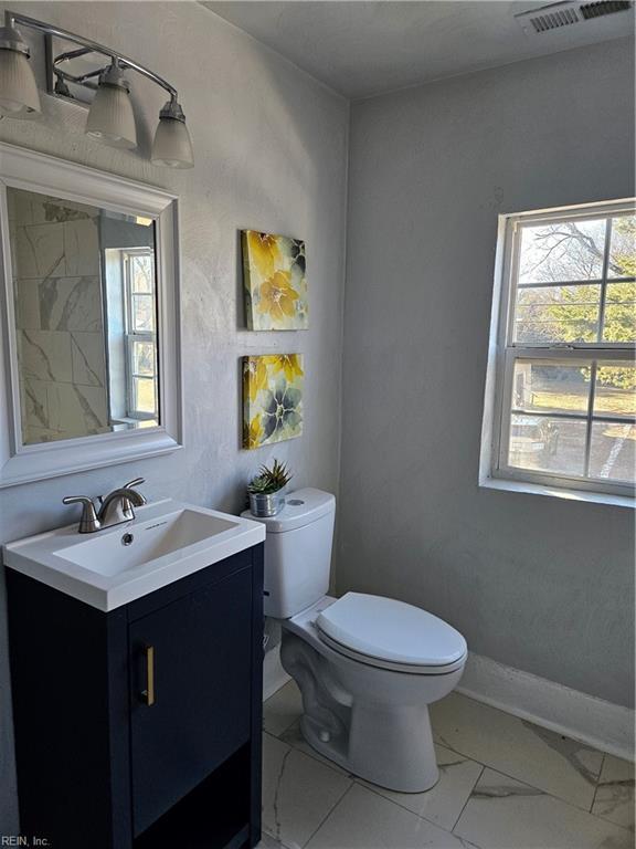half bathroom with toilet, marble finish floor, vanity, and a wealth of natural light