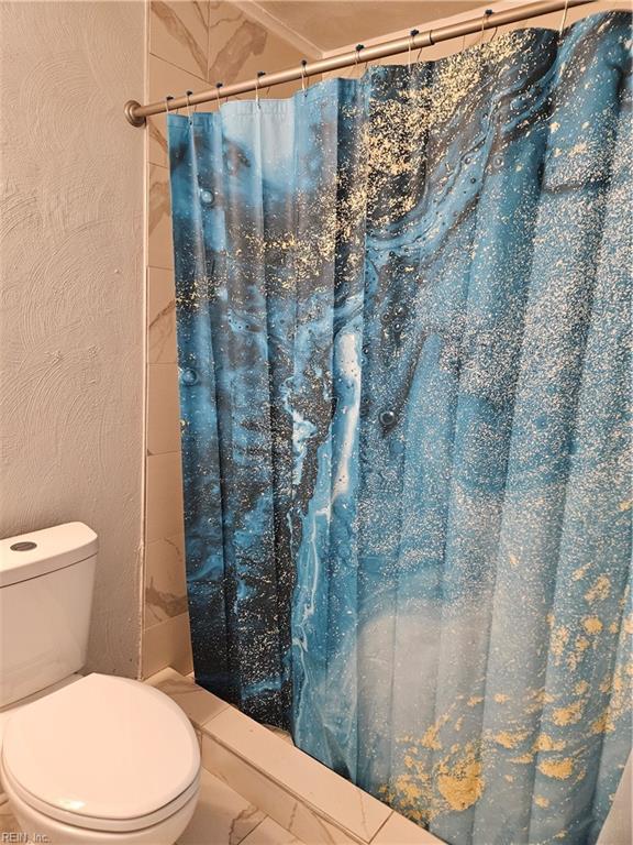 bathroom featuring toilet, marble finish floor, and a shower stall