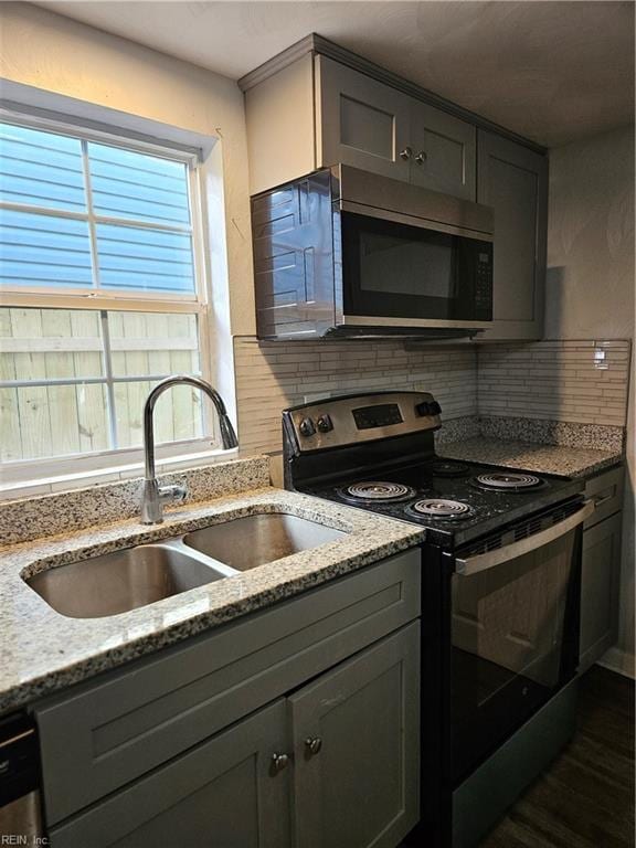 kitchen featuring a sink, appliances with stainless steel finishes, gray cabinetry, decorative backsplash, and light stone counters
