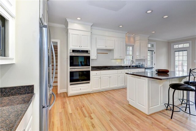 kitchen with a kitchen breakfast bar, ornamental molding, appliances with stainless steel finishes, a sink, and light wood finished floors