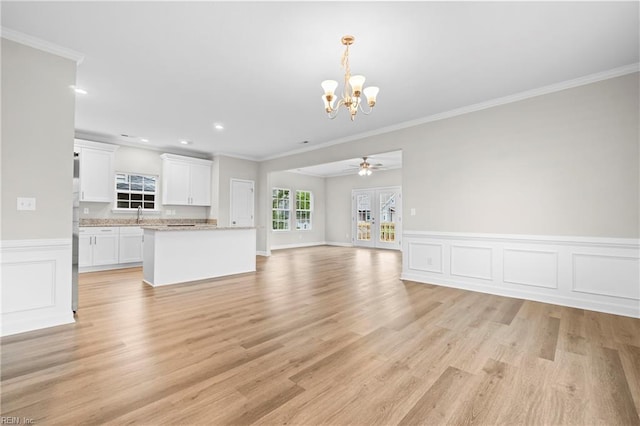 unfurnished living room featuring crown molding, a wainscoted wall, a chandelier, and light wood-style floors