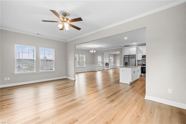 unfurnished living room featuring baseboards, light wood-type flooring, ceiling fan with notable chandelier, and ornamental molding