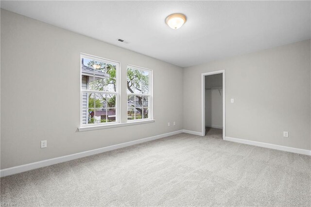 unfurnished bedroom with a spacious closet, visible vents, baseboards, and light carpet
