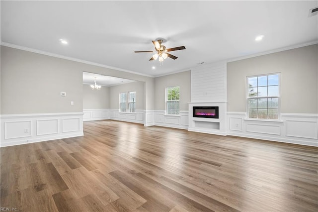 unfurnished living room with ornamental molding, a healthy amount of sunlight, a glass covered fireplace, and ceiling fan with notable chandelier