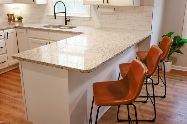 kitchen with light wood-style floors, a kitchen bar, a peninsula, white cabinets, and a sink