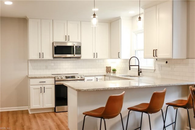 kitchen featuring a sink, light wood-type flooring, appliances with stainless steel finishes, a peninsula, and white cabinetry