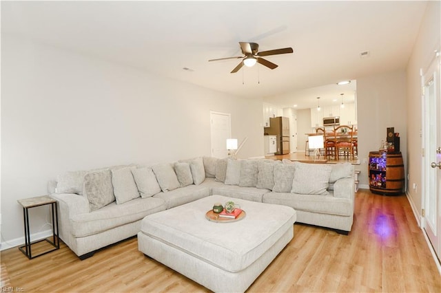 living room featuring light wood-style floors, baseboards, and a ceiling fan