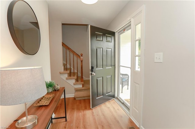 foyer entrance featuring light wood-style floors, baseboards, and stairway