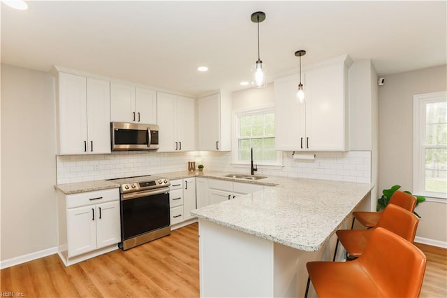 kitchen featuring a sink, light wood-type flooring, a peninsula, white cabinetry, and stainless steel appliances