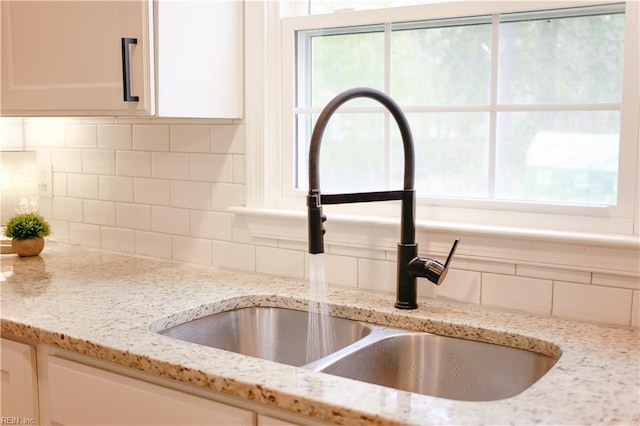 details with tasteful backsplash, light stone counters, a sink, and white cabinetry