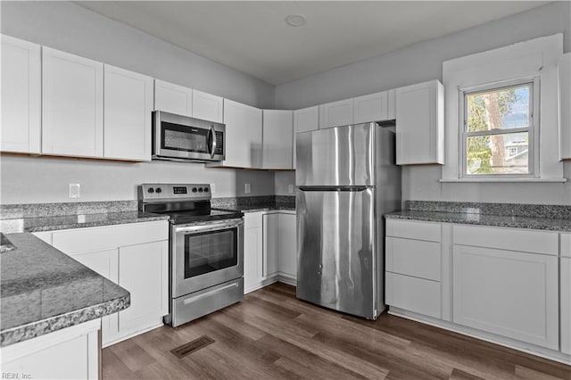 kitchen with dark stone counters, white cabinets, visible vents, stainless steel appliances, and dark wood-style floors