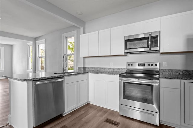 kitchen with white cabinets, a sink, appliances with stainless steel finishes, a peninsula, and dark wood-style floors