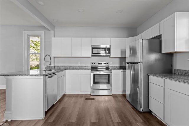 kitchen featuring appliances with stainless steel finishes, a peninsula, white cabinetry, dark wood finished floors, and a sink