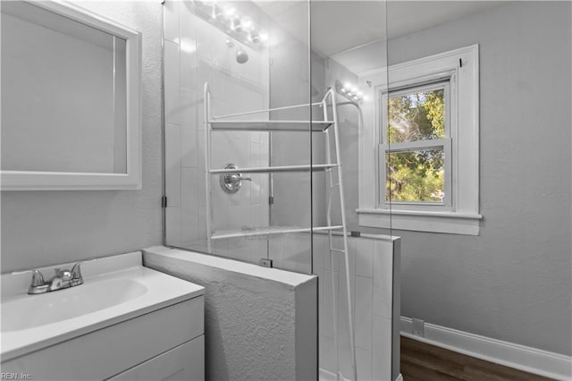 full bath with tiled shower, vanity, and wood finished floors