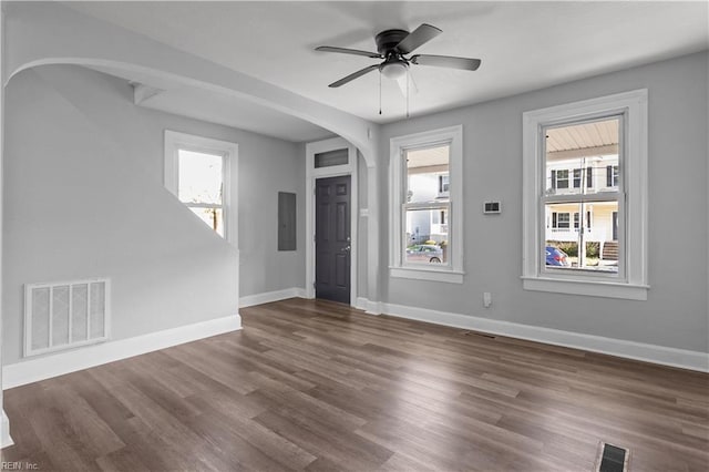 empty room with arched walkways, baseboards, dark wood finished floors, and visible vents