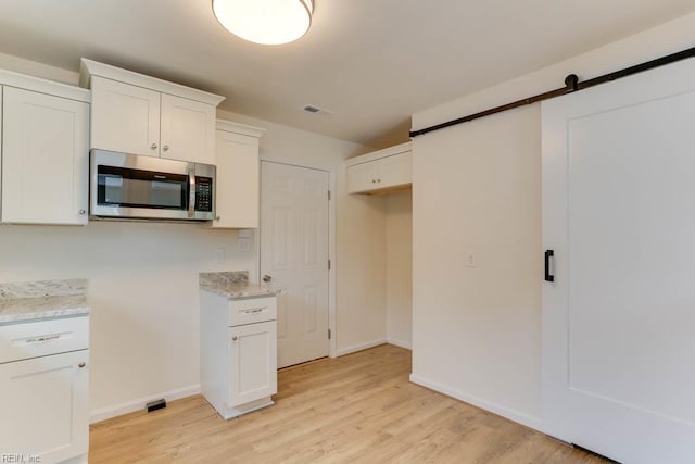 1793 Old Buckroe Rd, Hampton, VA 23664 - kitchen featuring light wood-style floors, white cabinetry, a barn door, stainless steel microwave, and baseboards