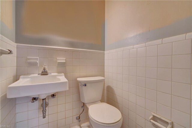half bath with a sink, tile walls, and toilet