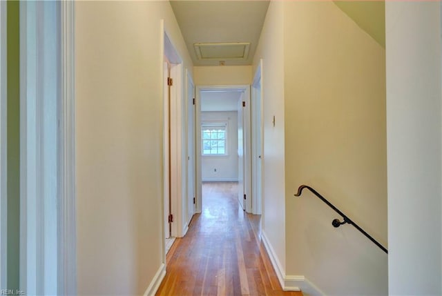 corridor featuring light wood-style flooring, an upstairs landing, and baseboards