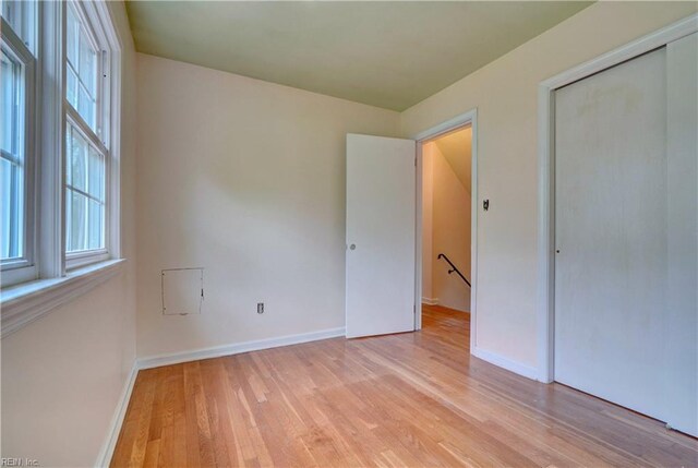 unfurnished bedroom with a closet, baseboards, multiple windows, and light wood-style floors