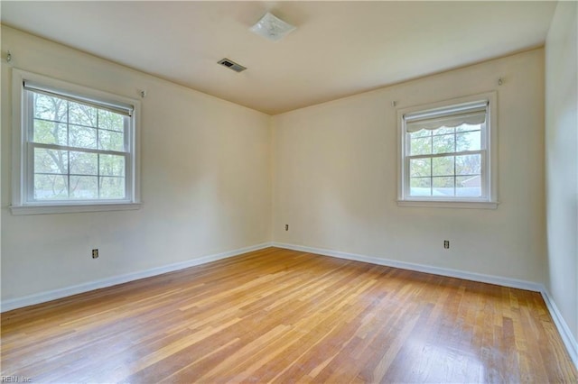unfurnished room with visible vents, light wood-style flooring, a wealth of natural light, and baseboards