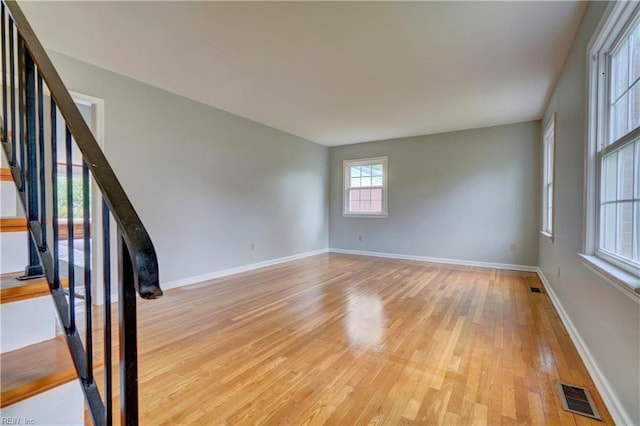 empty room featuring light wood-type flooring, baseboards, visible vents, and stairs