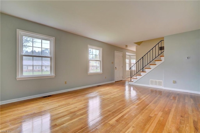 unfurnished living room with light wood finished floors, baseboards, visible vents, and stairway