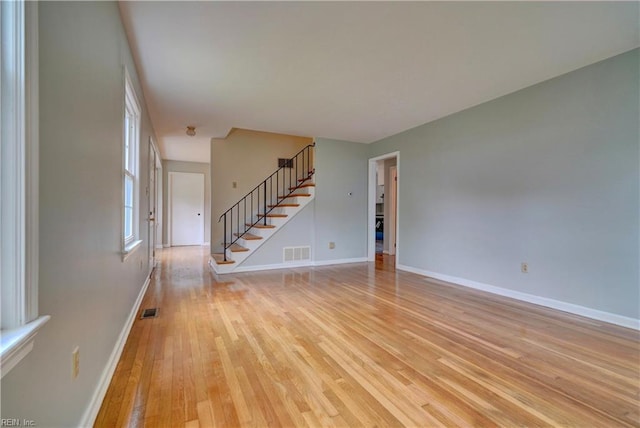 unfurnished living room featuring visible vents, baseboards, stairway, and light wood-style floors