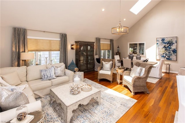 living room featuring a chandelier, high vaulted ceiling, a skylight, and a healthy amount of sunlight