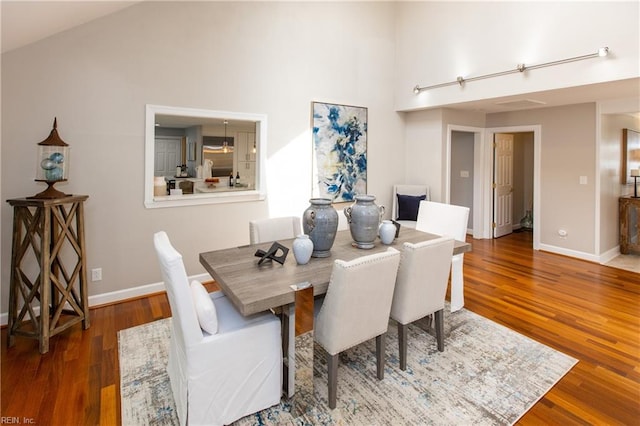 dining space with high vaulted ceiling, baseboards, and wood finished floors