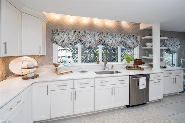 kitchen featuring stainless steel dishwasher, white cabinets, a sink, and decorative backsplash