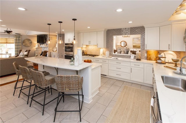 kitchen with a kitchen bar, tasteful backsplash, white cabinets, a sink, and open floor plan
