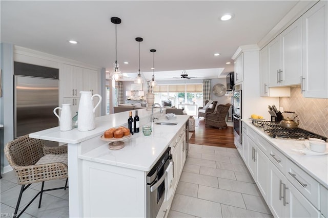 kitchen with tasteful backsplash, a sink, open floor plan, white cabinetry, and stainless steel appliances