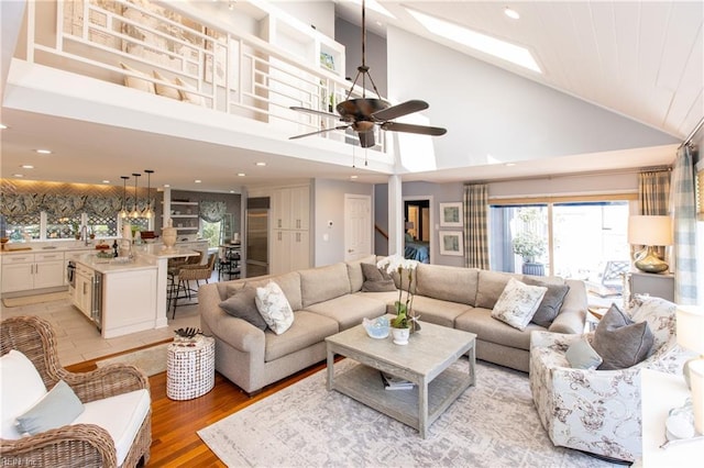 living area with light wood-type flooring, recessed lighting, a ceiling fan, a skylight, and high vaulted ceiling