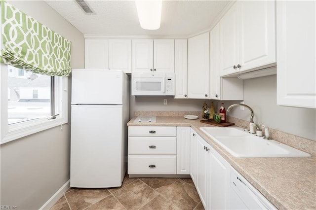 kitchen featuring white appliances, light countertops, white cabinetry, visible vents, and a sink