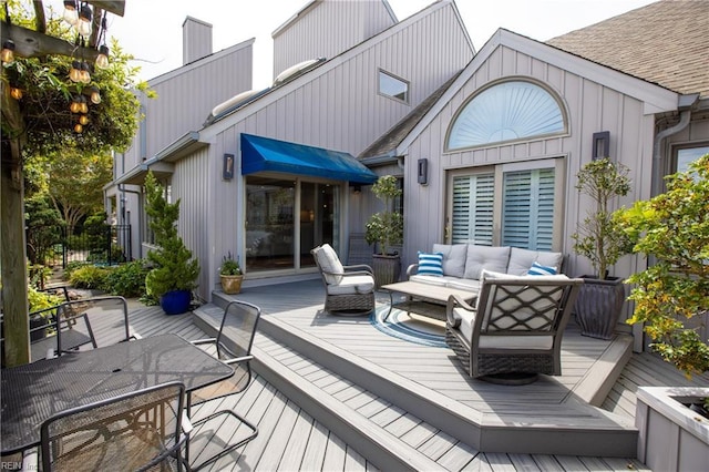 rear view of house featuring a chimney, outdoor dining area, a wooden deck, an outdoor hangout area, and a shingled roof