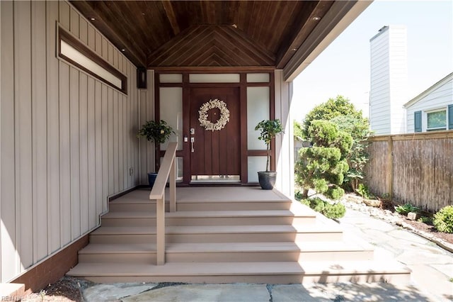 view of exterior entry with board and batten siding and fence