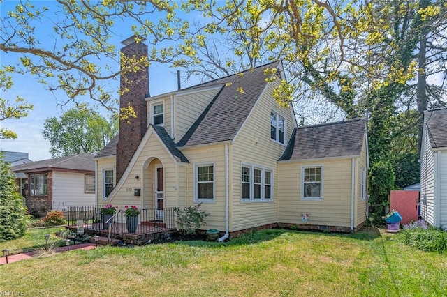 view of front facade with roof with shingles, a front lawn, and a chimney