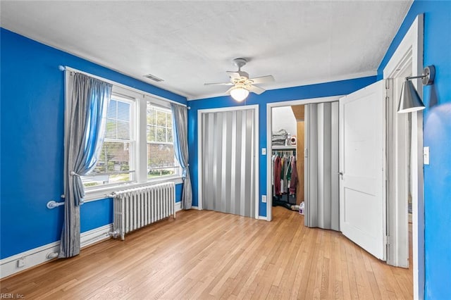 unfurnished bedroom with a ceiling fan, two closets, radiator heating unit, visible vents, and hardwood / wood-style floors