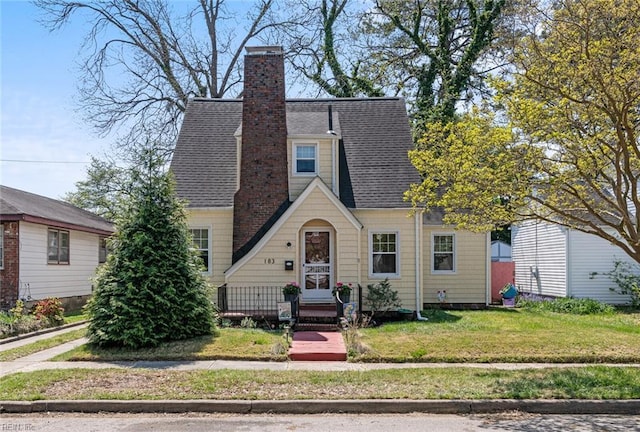 view of front of home with a chimney, a shingled roof, and a front yard