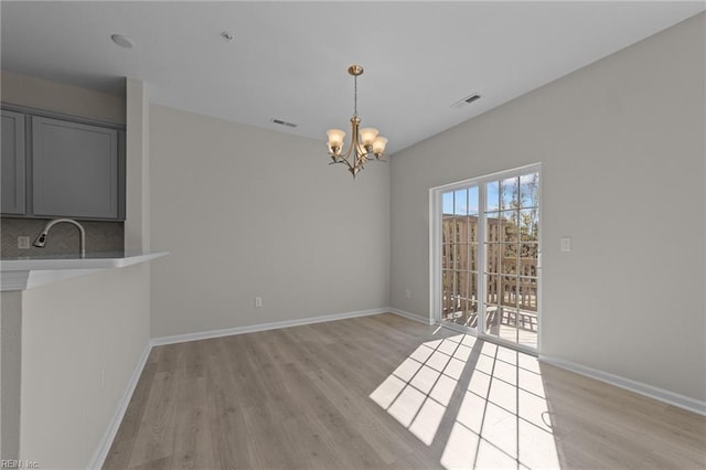 unfurnished dining area with visible vents, baseboards, light wood-type flooring, and an inviting chandelier