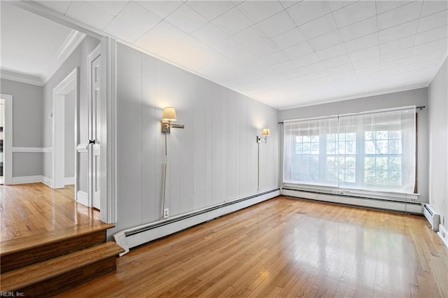 empty room with ornamental molding, a baseboard heating unit, wood finished floors, and baseboard heating