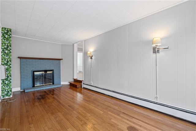 unfurnished living room with ornamental molding, hardwood / wood-style floors, a baseboard heating unit, and a fireplace